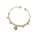 Gold tone round eye open cuff bracelet on white, with concentric blue and clear accents and four small dangling eye charms.