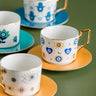 White cup with blue hearts, circular eyes and crescent moons on a yellow saucer, viewed from above