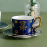 Navy cup with gold tone Namaste lettering, lotus flowers, Om symbols and a Hamsa eye motif on a dark saucer