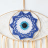 Close-up of the blue, white, turquoise and black eye motif inside a tan dream catcher frame