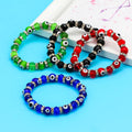 Black, blue, green and red evil eye beaded bracelets arranged on a turquoise background