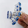 Hand holding a clear five-eye hair claw clip, showing blue motifs, curved teeth and the spring hinge