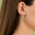 Gold tone evil eye and Hamsa chain-drop earring worn beside a separate hoop
