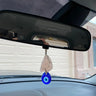 Blue evil eye teardrop beneath a pale pink accent, suspended from a car rearview mirror