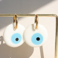 White round evil eye earrings with light blue centers and gold tone hoops hanging on a display bar