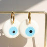 White round evil eye earrings with light blue centers and gold tone hoops hanging on a display bar