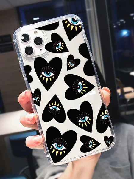 Hand holding an iPhone case with black heart motifs, blue and white eyes, yellow rays and clear edges, viewed from the back.