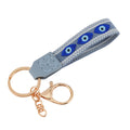 Grey loop keychain with three almond-shaped blue eyes, white patterned borders and gold tone attachments.