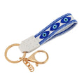 White loop keychain with three almond-shaped blue eyes, blue patterned borders and gold tone attachments.