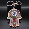 Brown Hamsa keychain with green flowers and a blue Evil Eye, displayed front-facing with its keyring and clasp above.