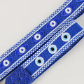 Close-up of royal blue straps with almond-shaped and round eye motifs between white patterned borders.