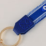 Close-up of a blue end tab with X-shaped stitches connecting an eye-patterned strap to a gold tone ring.