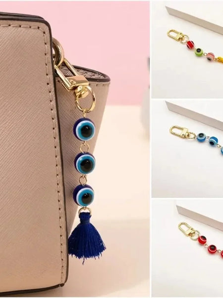 Dark blue evil eye tassel keychain clipped to a beige handbag, alongside inset views of multicolored, light blue and red versions.