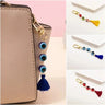 Dark blue evil eye tassel keychain clipped to a beige handbag, alongside inset views of multicolored, light blue and red versions.