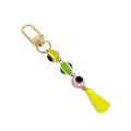 Multicolored evil eye keychain with yellow, green and pink beads, a yellow tassel and a gold tone clip on white.