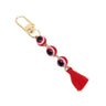Red evil eye keychain with three round beads, white eye rings, a red tassel and a gold tone clip on white.