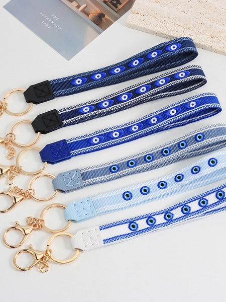 Six evil eye loop keychains in blue, grey and white, laid out with gold tone rings and clasps.