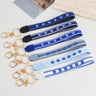 Six evil eye loop keychains in blue, grey and white, laid out with gold tone rings and clasps.