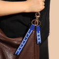 Two royal blue evil eye loop keychains with different eye patterns hanging beside a brown bag.