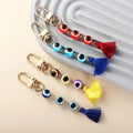 Red, light blue, multicolored and dark blue evil eye tassel keychains arranged beside a grey ridged display.