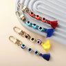 Red, light blue, multicolored and dark blue evil eye tassel keychains arranged beside a grey ridged display.