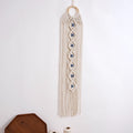 Off-white macrame hanging with seven blue eyes and long fringe above a partially visible tray and cord spools