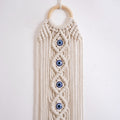 Upper section of the macrame hanging showing a pale tan ring and blue eyes within off-white diamond-shaped knots