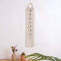 Macrame wall hanging above a vase and cactus, with green leaves in the foreground