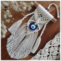 Angled view of the side-tassel evil eye hanging showing off-white knots around a blue pendant and separate twisted side cords.