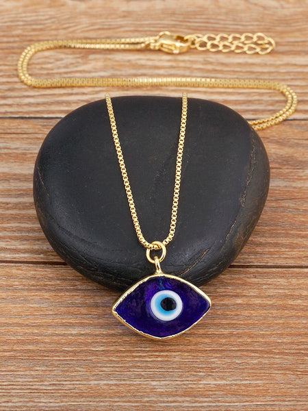 Dark blue evil eye necklace arranged over a black stone, showing the gold tone chain, pendant, clasp and extension links.