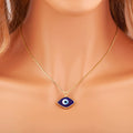 Dark blue eye-shaped pendant with a blue and white center on a gold tone chain, shown worn around a neck.