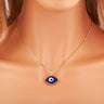 Dark blue eye-shaped pendant with a blue and white center on a gold tone chain, shown worn around a neck.