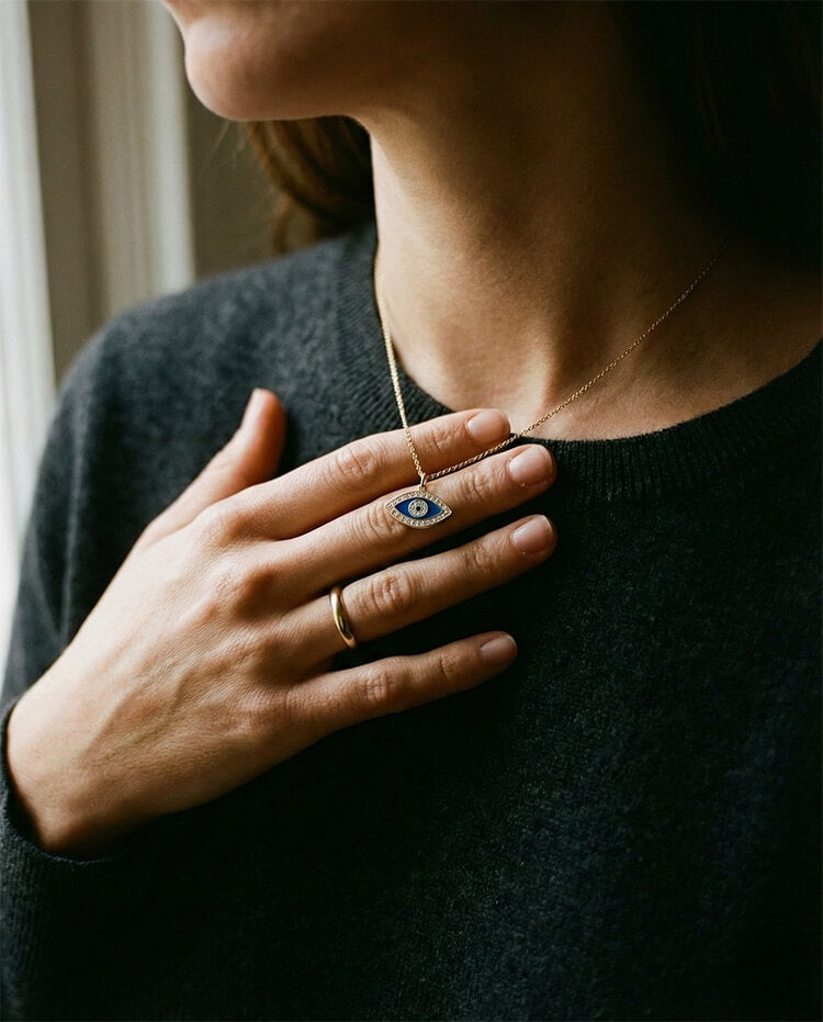 Woman gently touching a gold evil eye necklace, a daily ritual for calm and protection