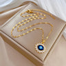 Gold tone oval link necklace laid out with a blue oval eye pendant surrounded by pointed clear accents.