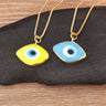 Yellow and light blue eye-shaped necklace pendants with blue and white centers and gold tone borders, displayed side by side.