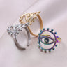 Three evil eye rings at different angles, showing the gold tone and silver tone bands beside the rainbow ring's oval face.