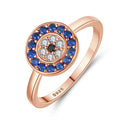 Angled view of a rose gold tone evil eye ring with a blue halo and clear petal-like accents around a black center
