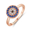 Angled view of a rose gold tone evil eye ring with a blue halo and clear petal-like accents around a black center