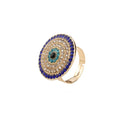 Gold tone evil eye ring with concentric blue and clear accents on a white background