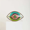 Patterned evil eye statue with pink loops around a green iris and turquoise and green sections.