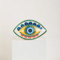 Evil eye statue with a yellow inner eye, blue upper petals, pink lower petals and a turquoise dotted border.