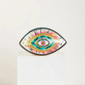 Patterned evil eye statue with a pink striped band, yellow inner outline and turquoise center.