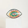 Patterned evil eye statue with a pink striped band, yellow inner outline and turquoise center.