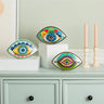 Three patterned evil eye statues displayed on a cabinet beside two candles.