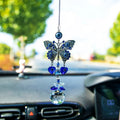 Butterfly evil eye suncatcher with blue heart charms and a clear faceted ball hanging in front of a car windshield
