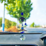 Blue eyelash eye suncatcher with a silver tone wing detail and clear faceted ball hanging in front of a car windshield