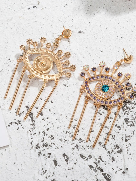 Gold tone evil eye fringe earrings showing an embellished front, textured reverse and straight posts on a speckled surface.
