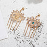 Gold tone evil eye fringe earrings showing an embellished front, textured reverse and straight posts on a speckled surface.