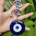 Round blue evil eye pendant and two silver tone eye motifs with curved lashes shown against a hand