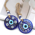 Two blue evil eye wall hangings with white daisies and colorful leafy branches around teardrop eye motifs